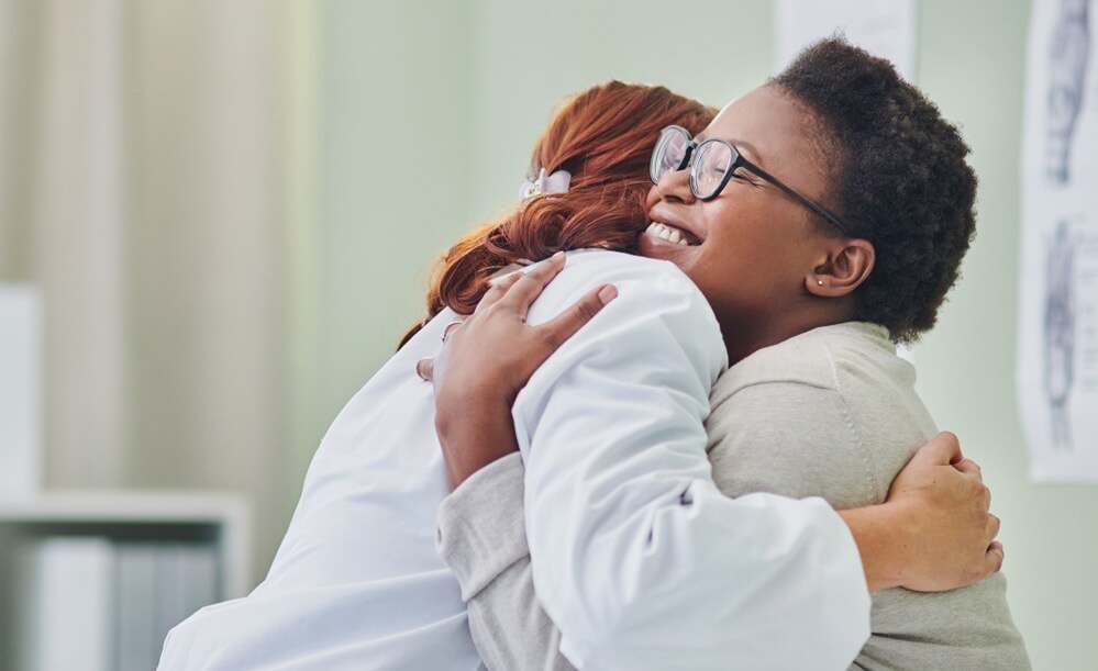 A female patient smiling and hugging a provider A female patient smiling and hugging a provider